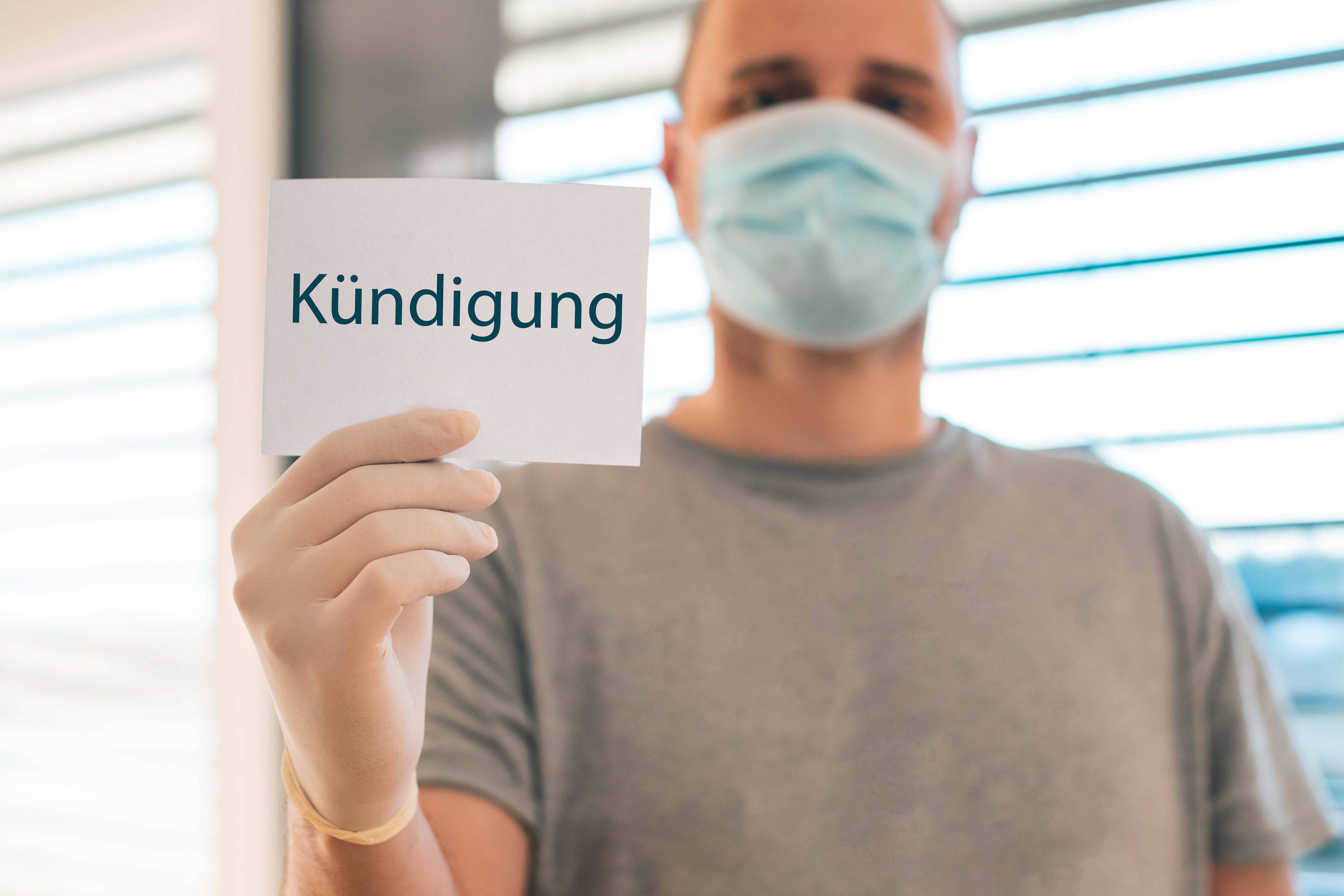 Person mit Maske hält Kündigungsschreiben
