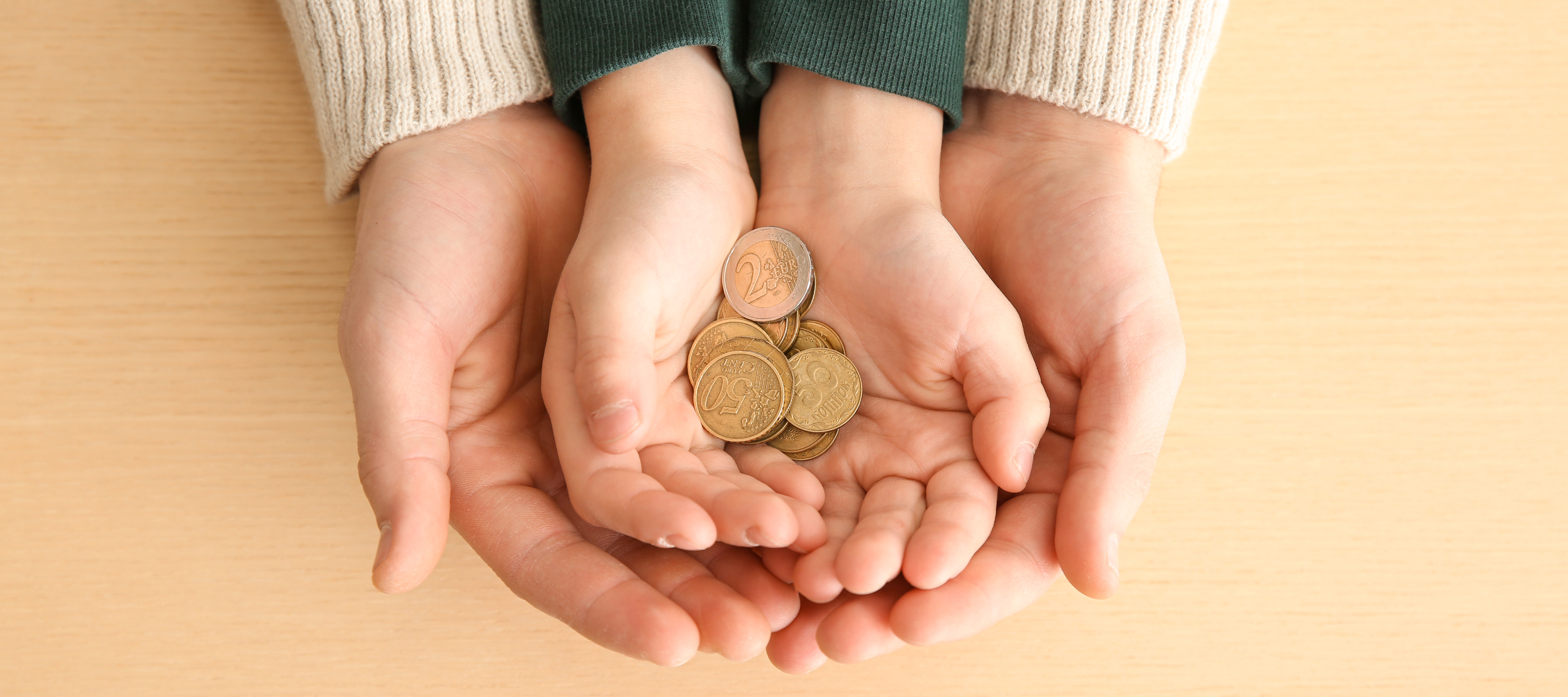 Kinderhände und Erwachsenenhände halten zusammen Euro-Münzen